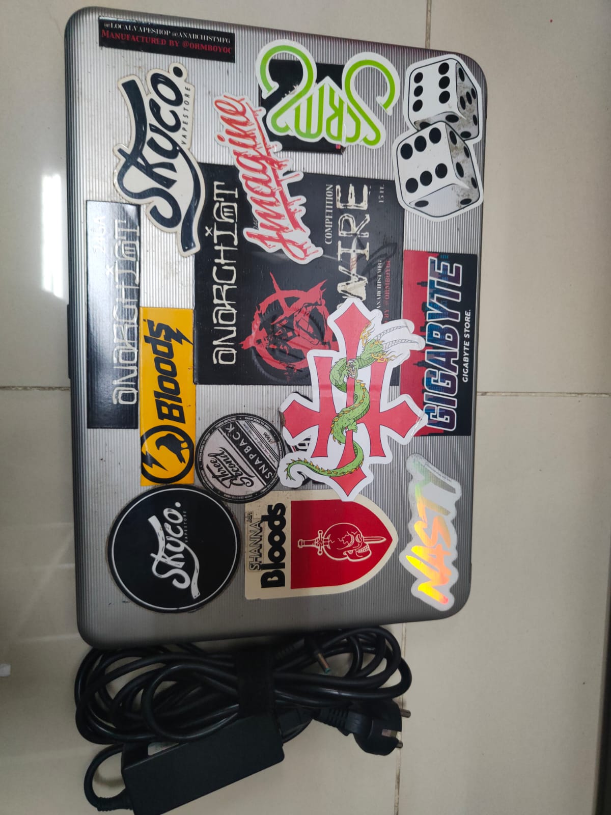 Laptop warna silver dengan berbagai macam stiker merk HP type TPN1120 beserta charger